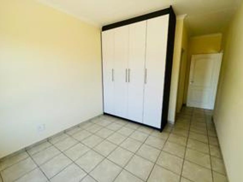 A clean, empty bedroom featuring neutral tiled flooring, a modern built-in wardrobe, and a classic white interior door.