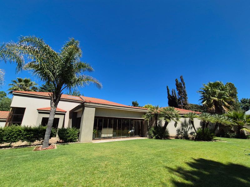 A well-maintained rear exterior view of the house featuring a spacious lawn, mature palm trees, and large sliding glass doors leading to the interior.