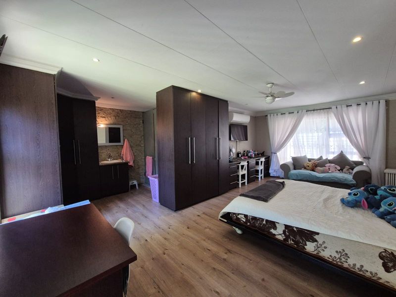 Spacious bedroom featuring laminate flooring, built-in cupboards, a ceiling fan, air conditioning, and an integrated vanity area with a stone feature wall.