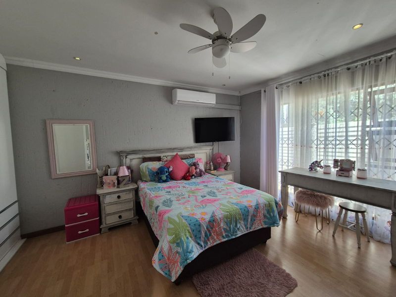 A well-maintained bedroom featuring laminate flooring, a ceiling fan, and a split-system air conditioner, with large windows protected by a security gate.