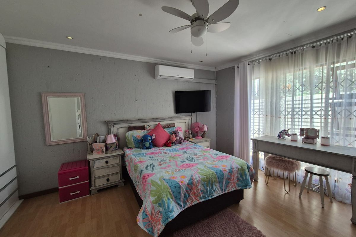 A well-maintained bedroom featuring laminate flooring, a ceiling fan, and a split-system air conditioner, with large windows protected by a security gate.