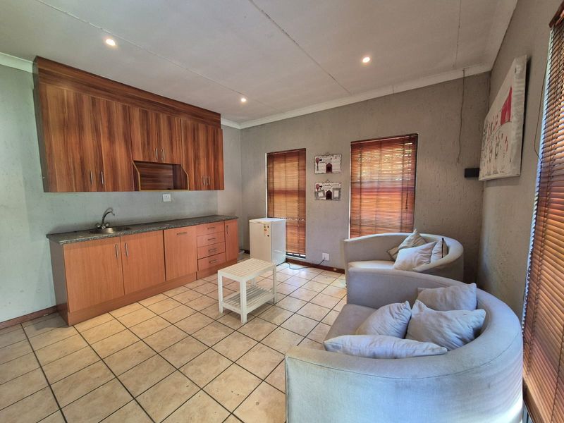 Open plan living area featuring a kitchenette with wood-finish cabinetry, tiled flooring, and large windows with fitted venetian blinds.