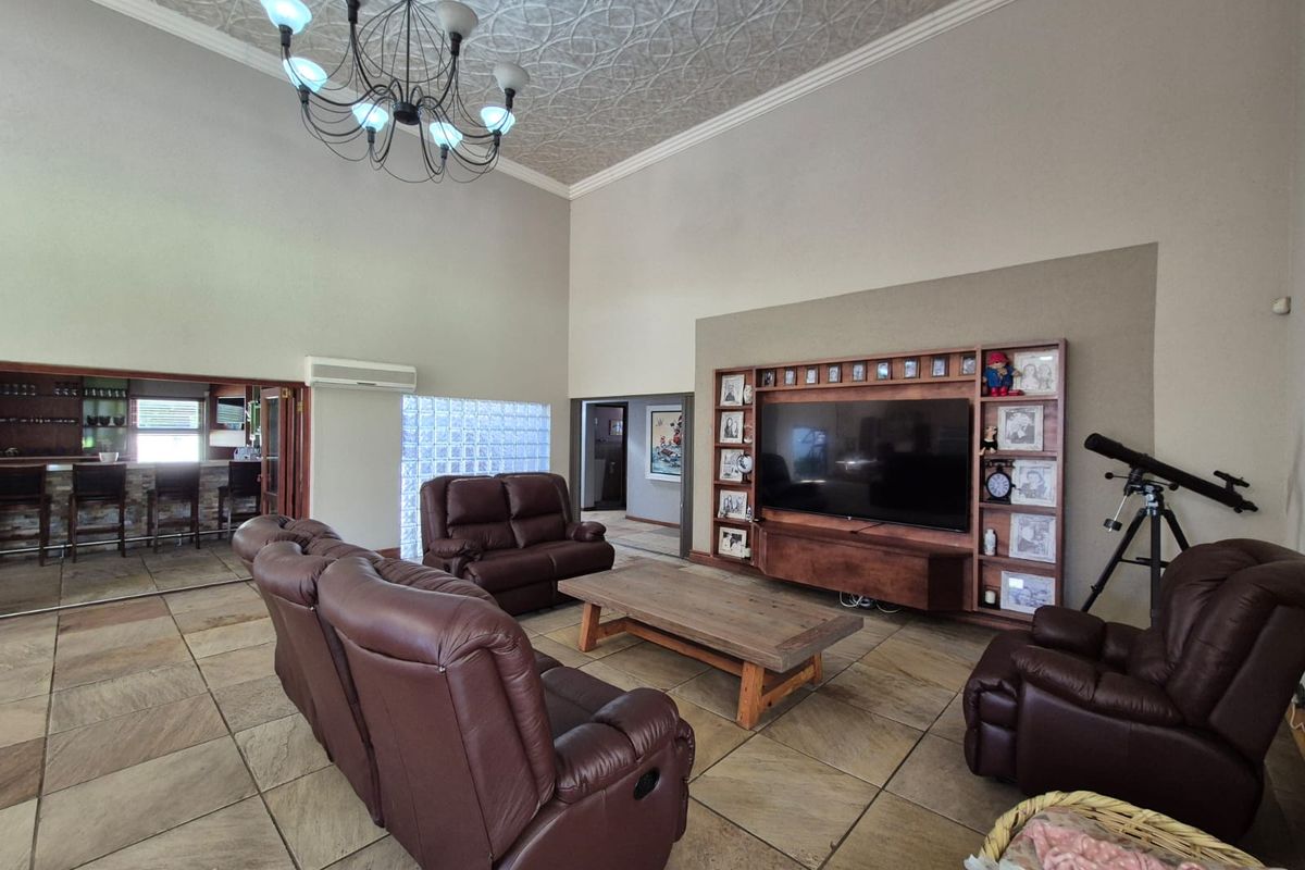 Spacious living room featuring high vaulted ceilings with decorative tiles, stone flooring, a built-in media wall, and a glass block feature window.