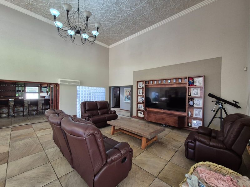 Spacious living room featuring high vaulted ceilings with decorative tiles, stone flooring, a built-in media wall, and a glass block feature window.