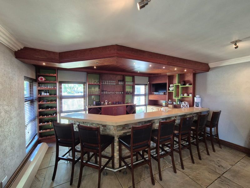 A well-appointed built-in home bar featuring custom cabinetry, stone-clad counter, integrated shelving, and recessed lighting, finished with durable tiled flooring.
