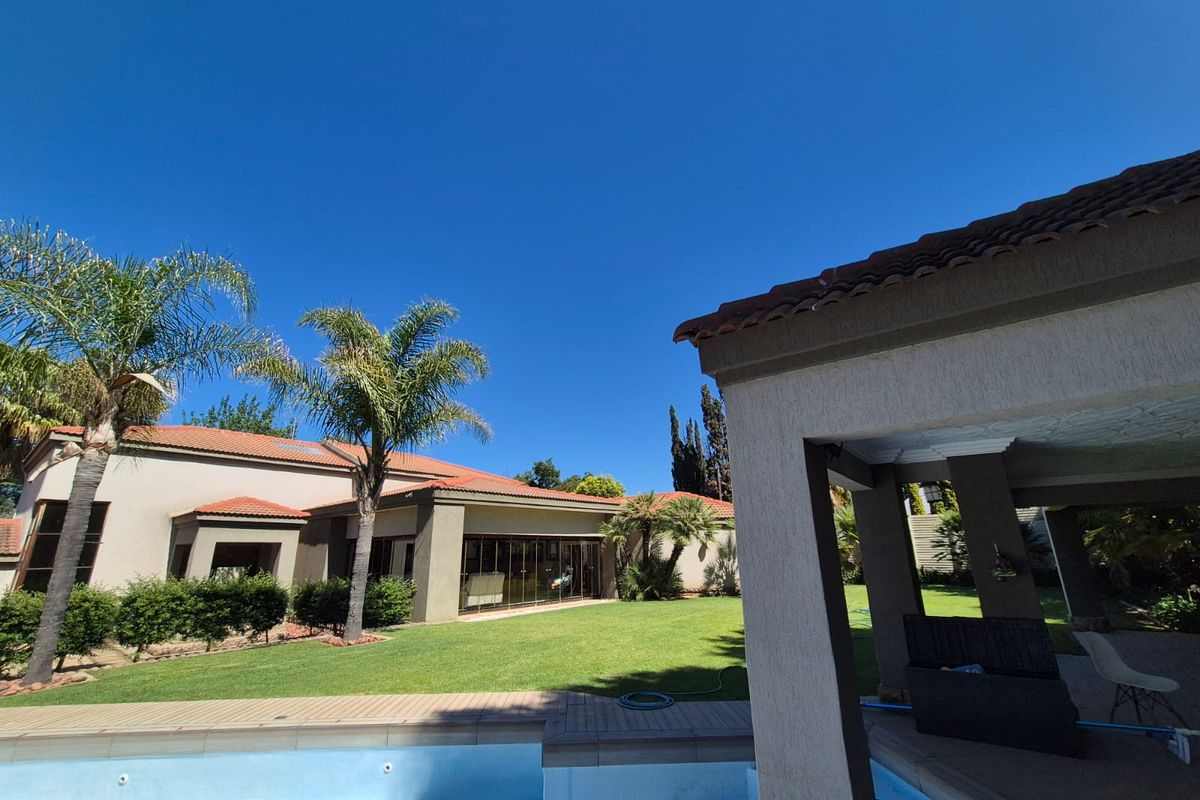 A spacious rear garden featuring a swimming pool, a covered patio area, and a well-maintained lawn with views of the main house structure.