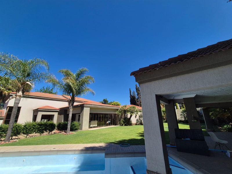 A spacious rear garden featuring a swimming pool, a covered patio area, and a well-maintained lawn with views of the main house structure.