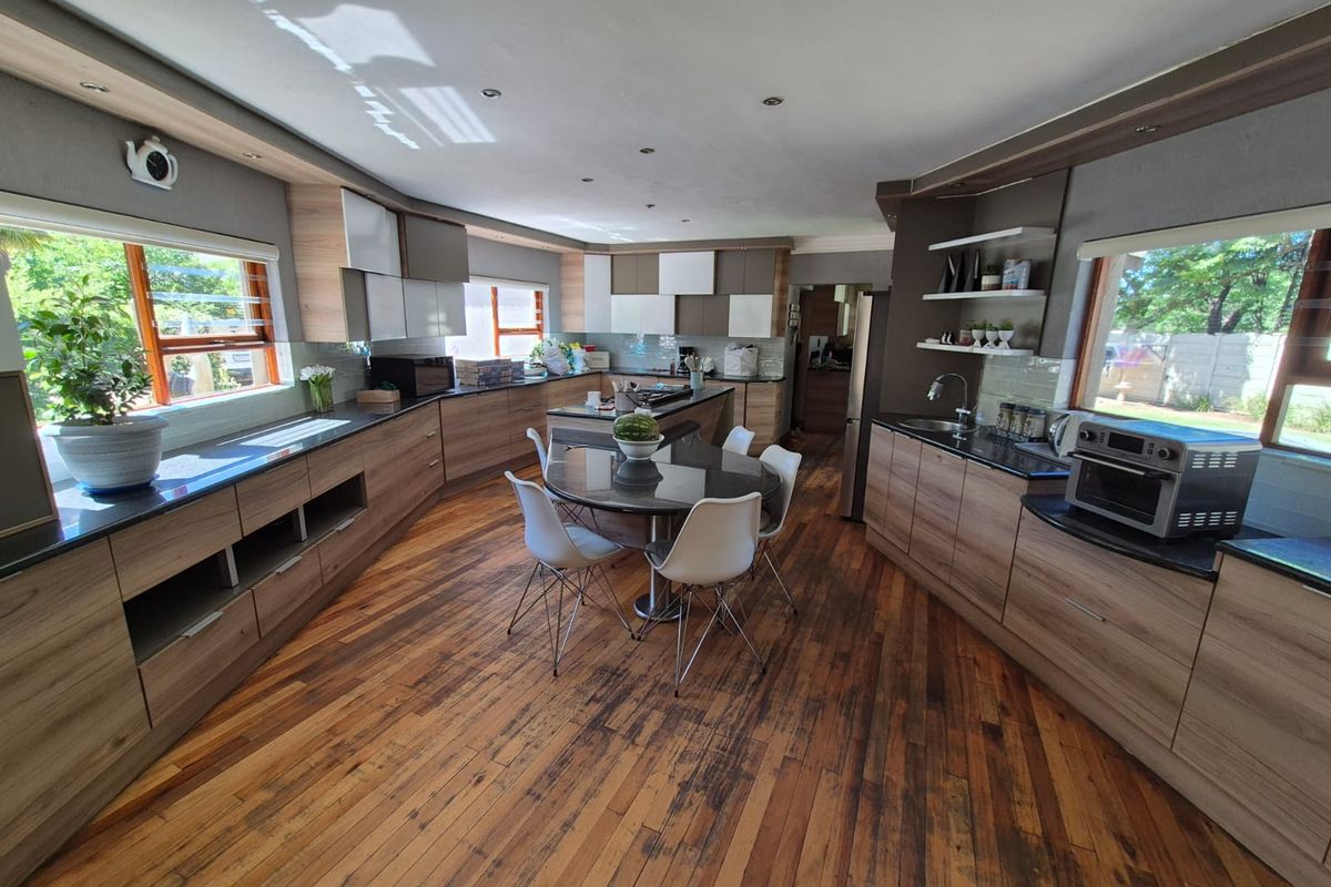 Spacious modern kitchen featuring extensive wood-grain cabinetry, stone countertops, a central island, and warm hardwood flooring with ample natural light.
