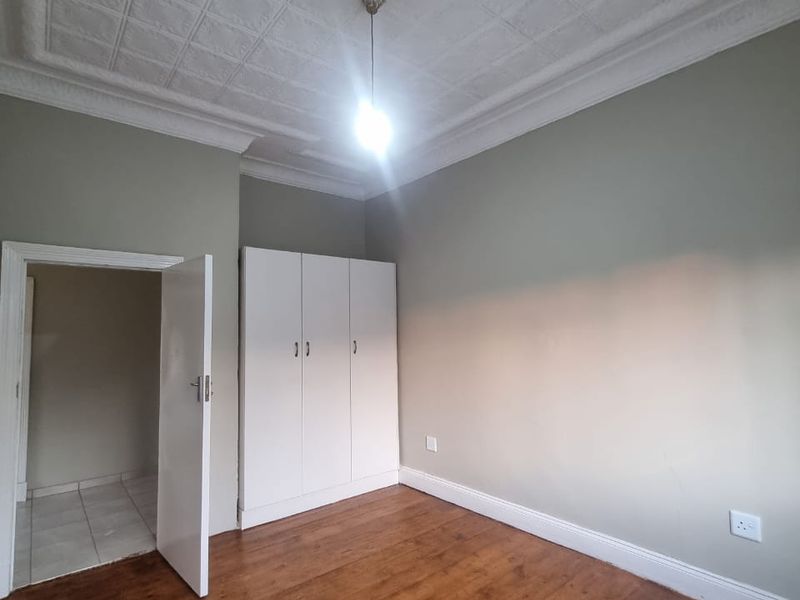 An empty bedroom featuring original pressed metal ceilings, timber flooring, and a built-in wardrobe.
