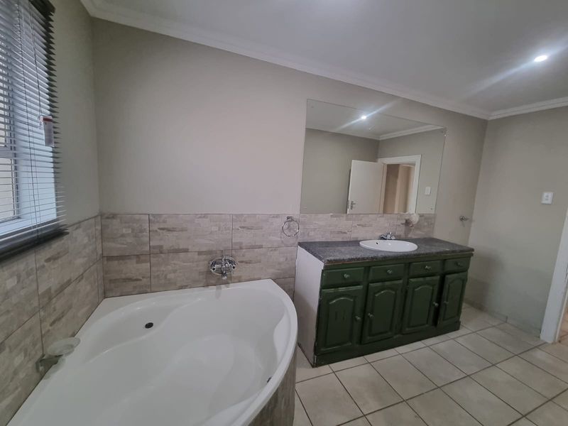 A functional bathroom featuring a corner bathtub, a vanity unit with a basin, and neutral wall tiling.