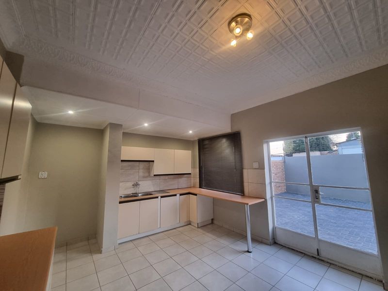 A functional kitchen featuring built-in cabinetry, a double basin sink, tiled flooring, and direct access to an outdoor paved area through a glass sliding door.