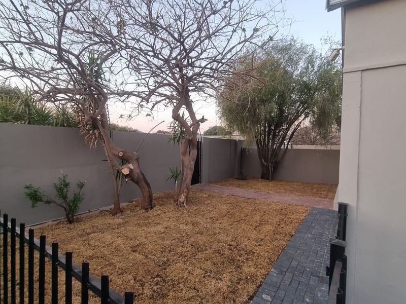 A compact garden area featuring a paved walkway, perimeter walling, and metal fencing, providing a private outdoor space.