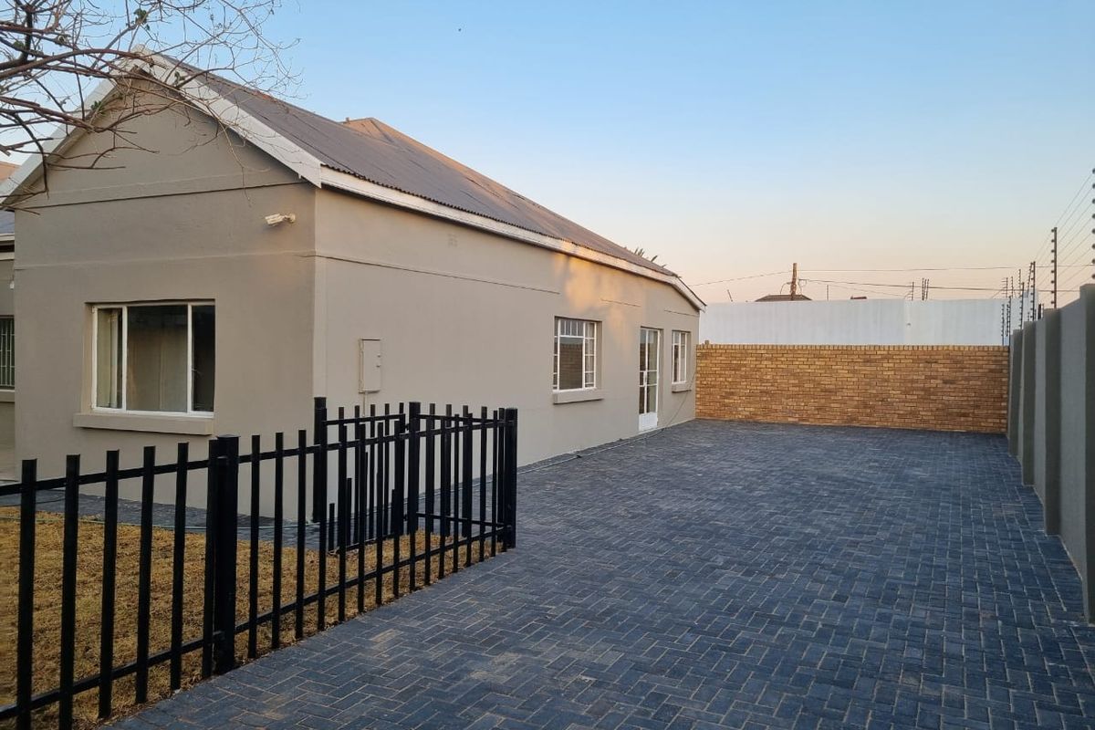A well-maintained rear exterior view featuring a paved driveway, secure metal fencing, and a clean brick boundary wall.