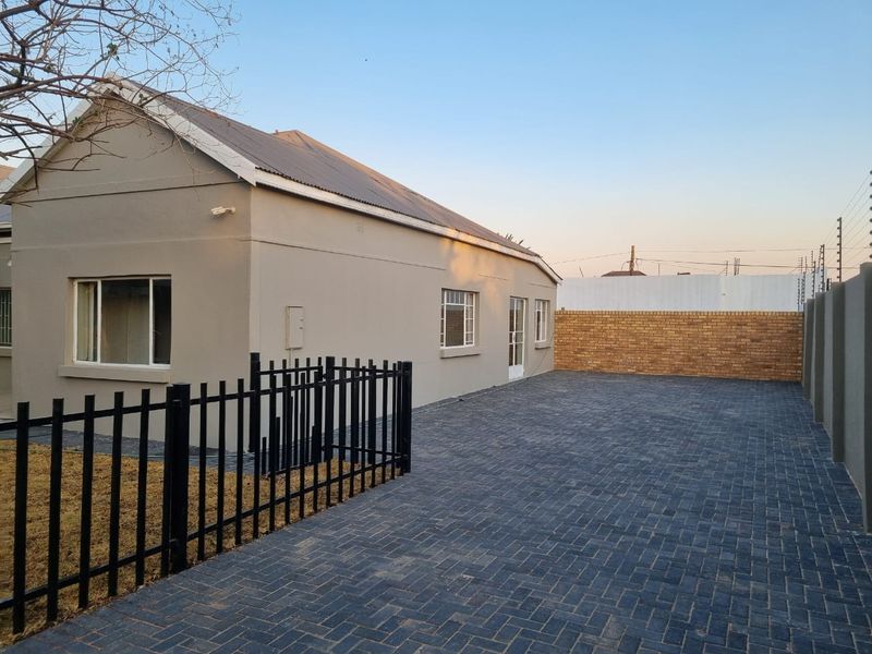 A well-maintained rear exterior view featuring a paved driveway, secure metal fencing, and a clean brick boundary wall.