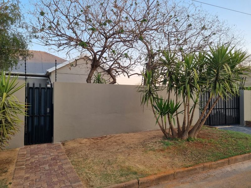Front exterior view featuring a solid perimeter wall, secure pedestrian and vehicle gates, electric fencing, and a paved walkway.