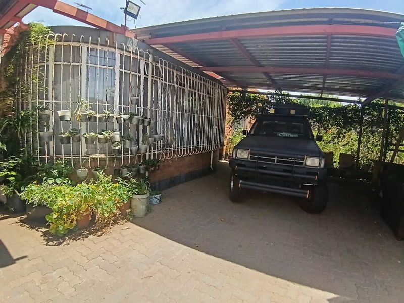 A covered carport area featuring a paved driveway and security bars on the adjacent building facade.