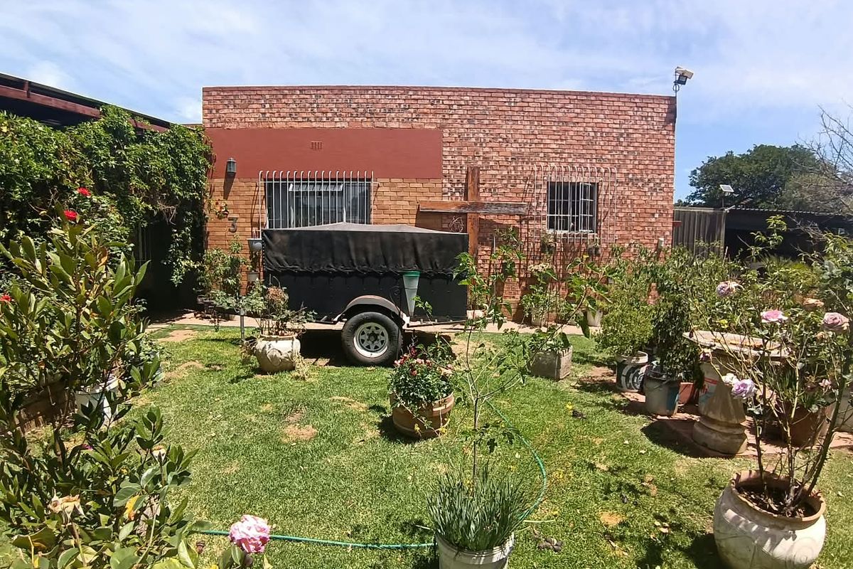Rear view of a face brick residential property featuring security bars on windows and a landscaped garden area.