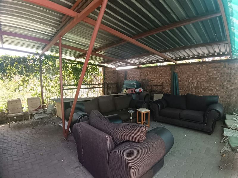 Covered outdoor patio area featuring a corrugated metal roof, steel support structure, and exposed brick wall with paved flooring.