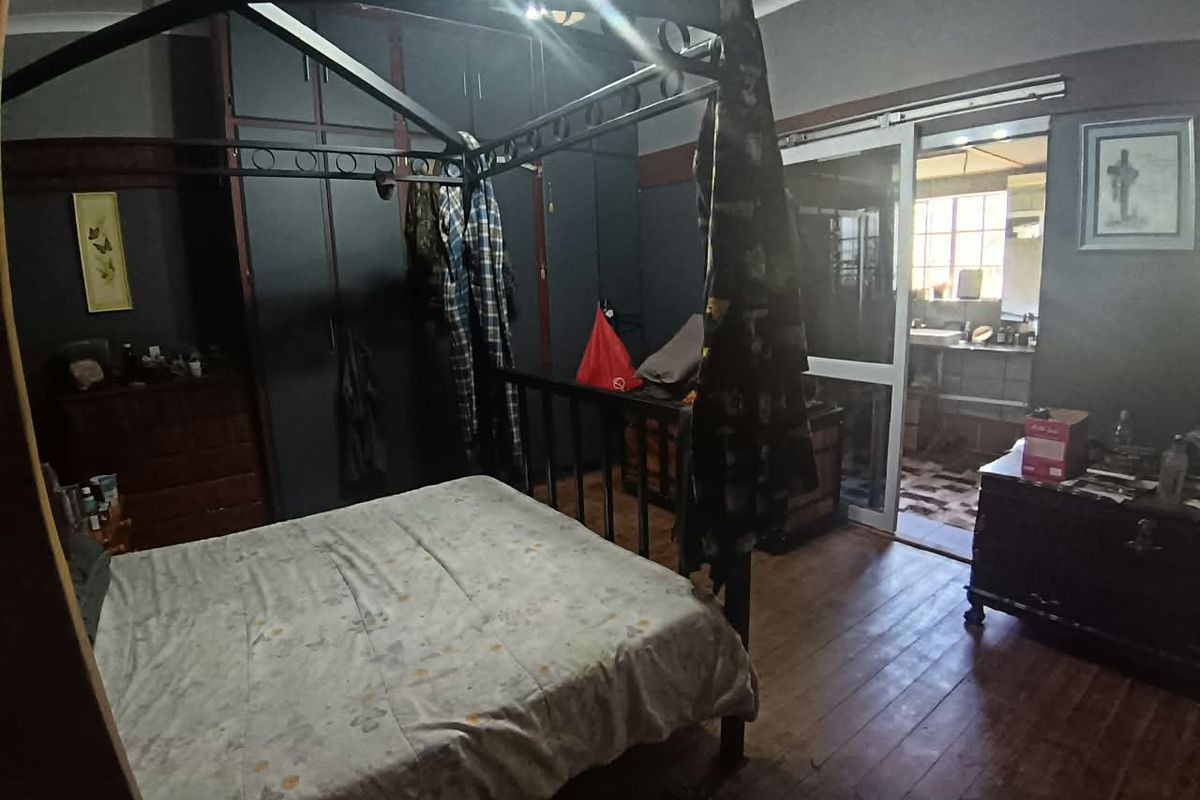 A bedroom featuring dark built-in cupboards, wooden flooring, and a sliding door leading to an adjacent room.