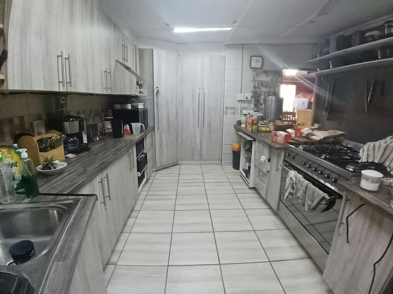 A functional kitchen featuring light wood-grain cabinetry, laminate countertops, a gas stove with oven, and tiled flooring throughout.