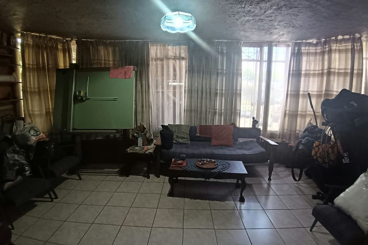 A living room area featuring tiled flooring and large windows, providing natural light. The space requires cosmetic updates to improve its overall condition.