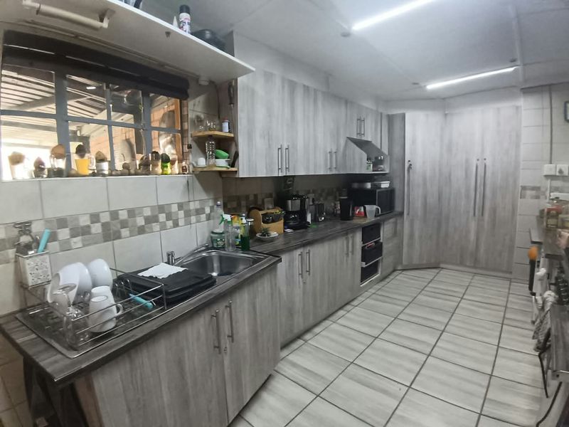 Functional kitchen featuring light wood-grain cabinetry, laminate countertops, tiled backsplash, and ample storage space with a built-in pantry.