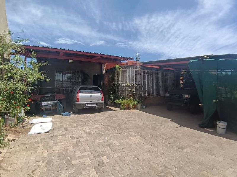 Front exterior view of the property featuring a paved driveway and a covered carport area with security bars on the windows.