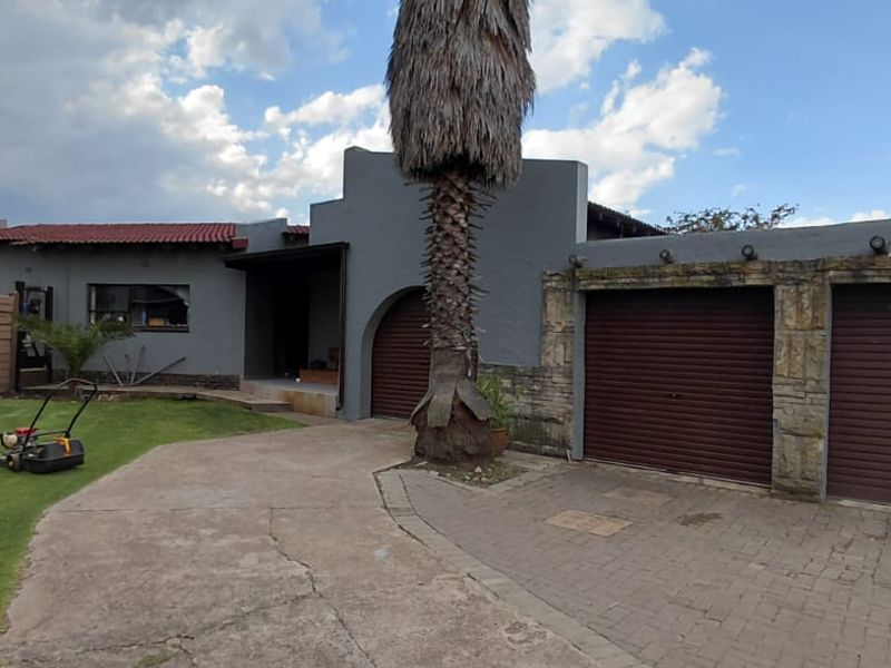 Front elevation of a house featuring a double garage with roller shutter doors, stone cladding accents, a paved driveway, and a front lawn.