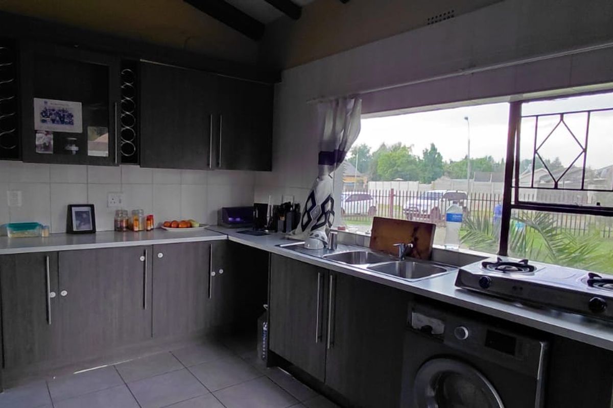 A functional kitchen featuring dark wood-look cabinetry, tiled flooring, a double sink, and a large window with security bars overlooking the exterior.