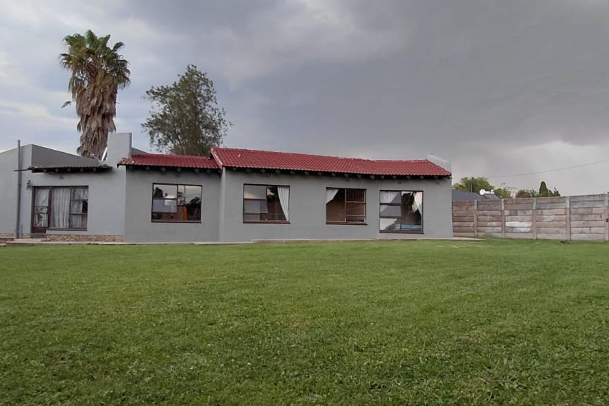 Rear view of the house featuring a large lawn, concrete boundary wall, and a red tiled roof with grey exterior walls.