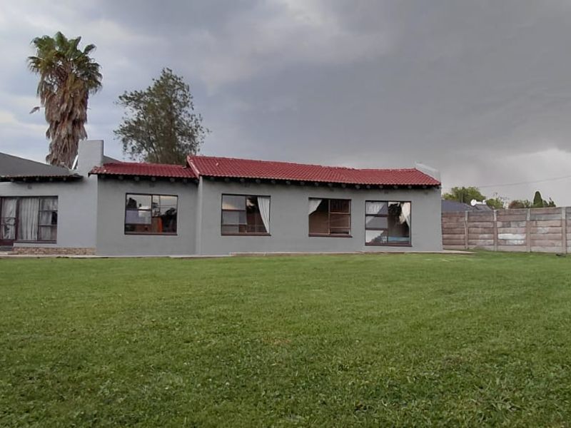 Rear view of the house featuring a large lawn, concrete boundary wall, and a red tiled roof with grey exterior walls.