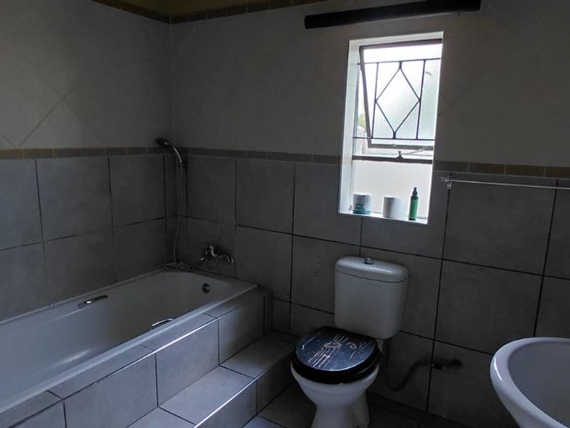 A functional bathroom featuring a built-in bathtub, pedestal basin, and toilet, finished with neutral ceramic wall and floor tiles.