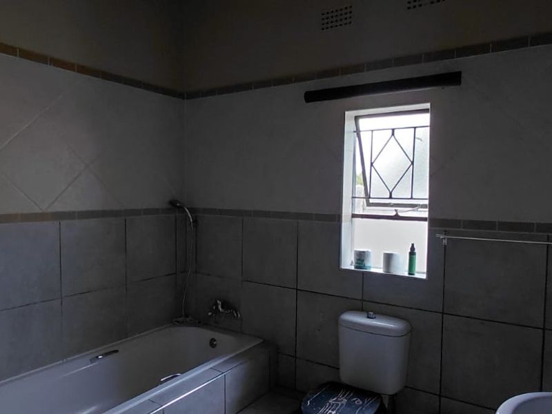 A functional bathroom featuring a bathtub, toilet, and washbasin with neutral wall tiling and a window for natural light.