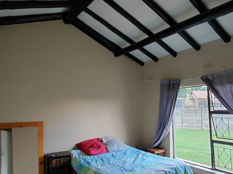 A bedroom featuring a vaulted ceiling with exposed timber beams, built-in cupboards, and a large window overlooking the garden.