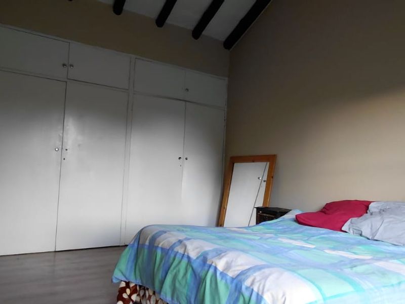 A bedroom featuring built-in cupboards, exposed ceiling beams, and laminate flooring, with an adjacent doorway leading to an en-suite area.