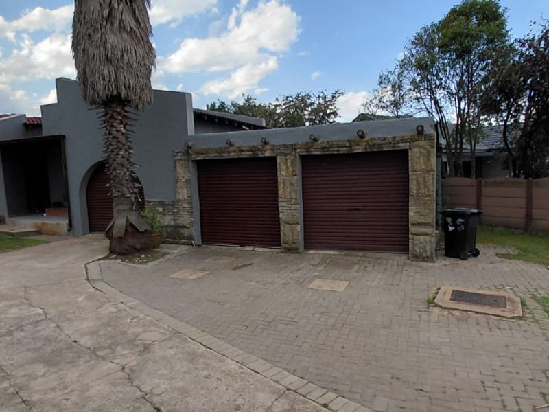 Front exterior view of the house featuring a double garage with roller shutter doors, stone cladding accents, and a paved driveway.