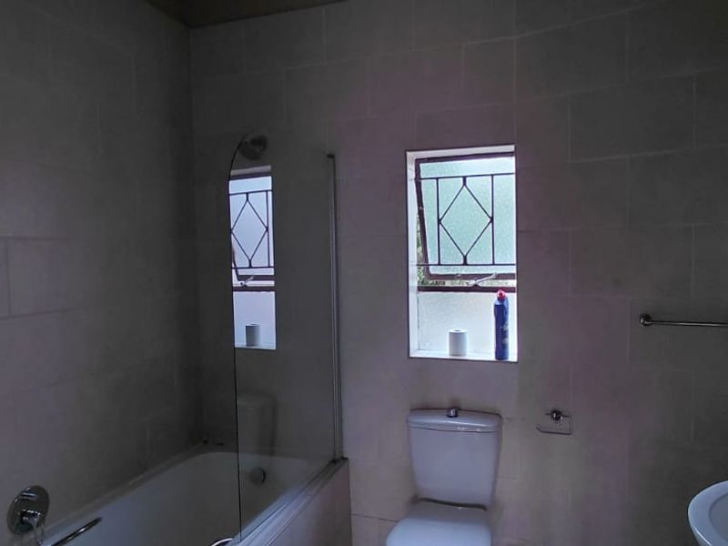 A functional bathroom featuring a bathtub with a glass screen, a pedestal basin, and a toilet, finished with neutral wall tiling.