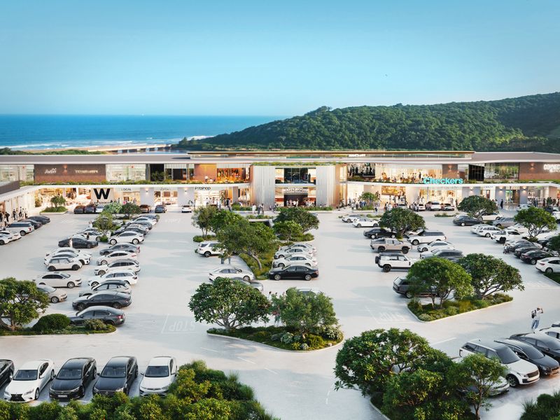 Aerial view of a modern commercial shopping center with extensive parking facilities, landscaped greenery, and a scenic coastal backdrop.