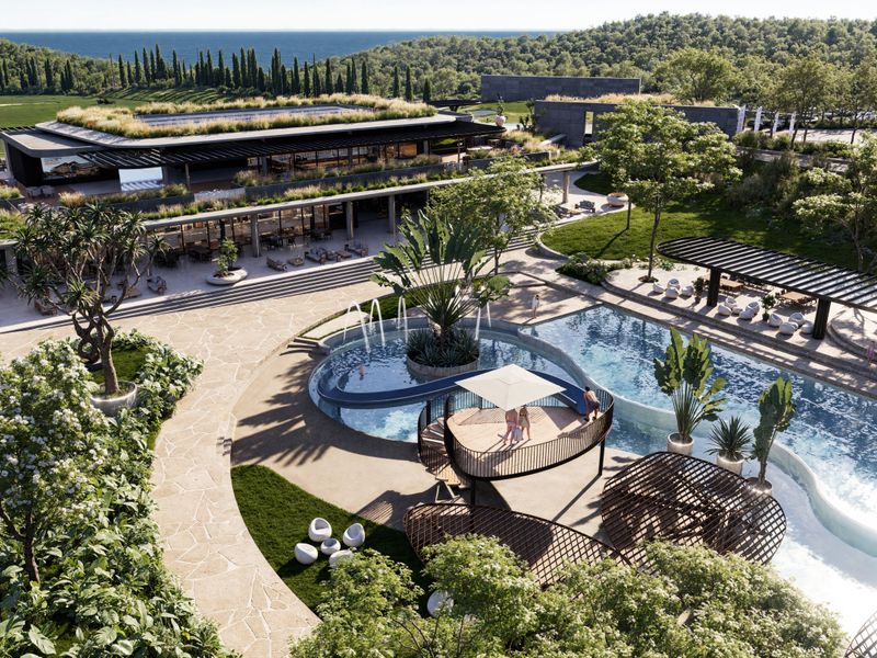 An expansive, modern outdoor leisure area featuring a large swimming pool, landscaped gardens, paved pathways, and a contemporary clubhouse with a green roof.