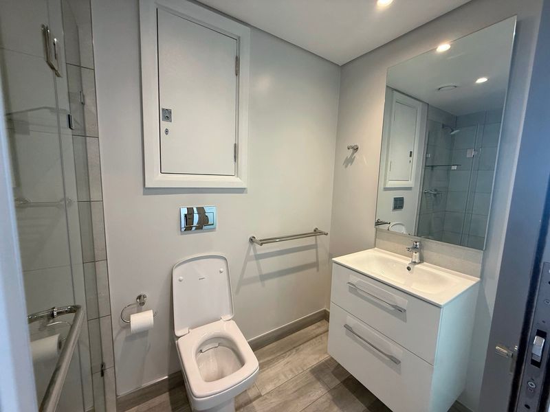 Modern bathroom featuring a wall-hung toilet with concealed cistern, vanity cabinet with integrated basin, and a glass-enclosed shower.