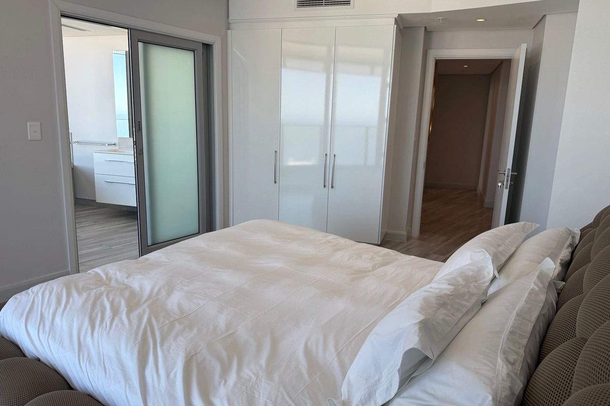 Modern bedroom featuring built-in high-gloss cupboards, ducted air conditioning, and direct access to an en-suite bathroom through a sliding glass door.