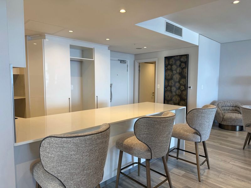 Modern open-plan living area featuring a sleek stone breakfast bar, recessed lighting, ducted air conditioning, and contemporary cabinetry with light wood-look flooring.