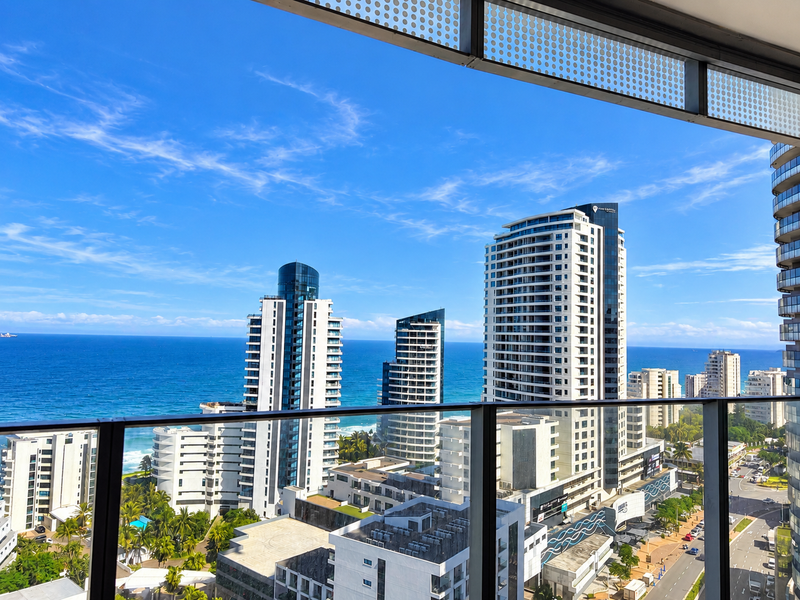 Stunning elevated coastal city and ocean view captured from a modern apartment balcony with a sleek glass balustrade.