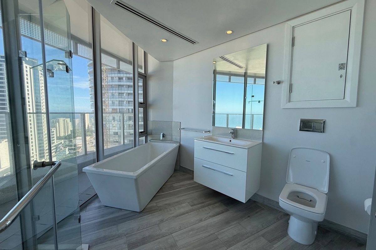 Modern, high-end bathroom featuring a freestanding bathtub, wall-mounted vanity, and glass shower enclosure with expansive city and sea views.