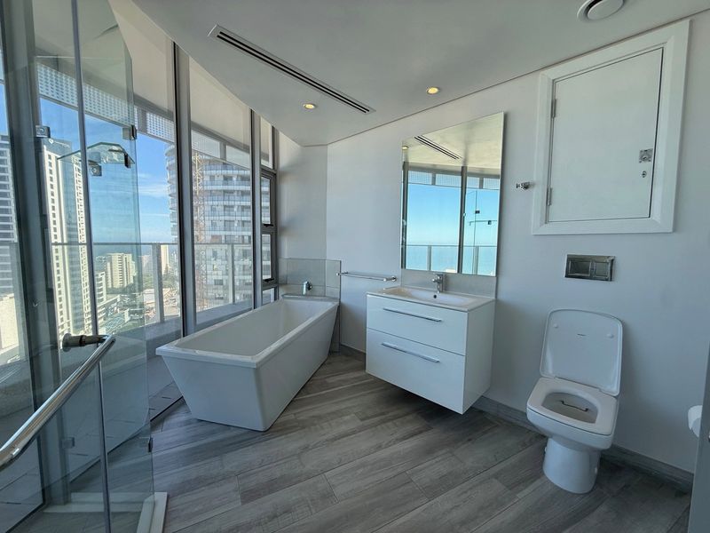 Modern, high-end bathroom featuring a freestanding bathtub, wall-mounted vanity, and glass shower enclosure with expansive city and sea views.