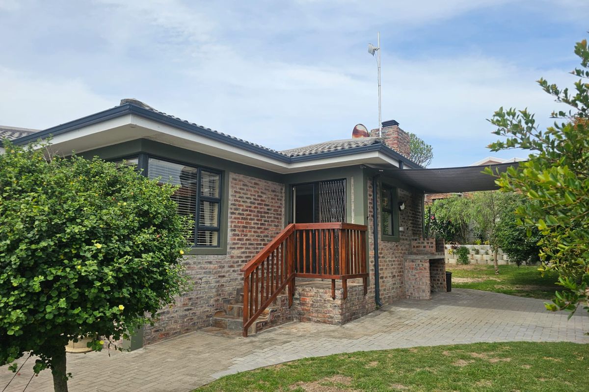 Rear view of the house featuring a face brick facade, paved patio area, built-in braai, and a wooden staircase leading to the entrance.
