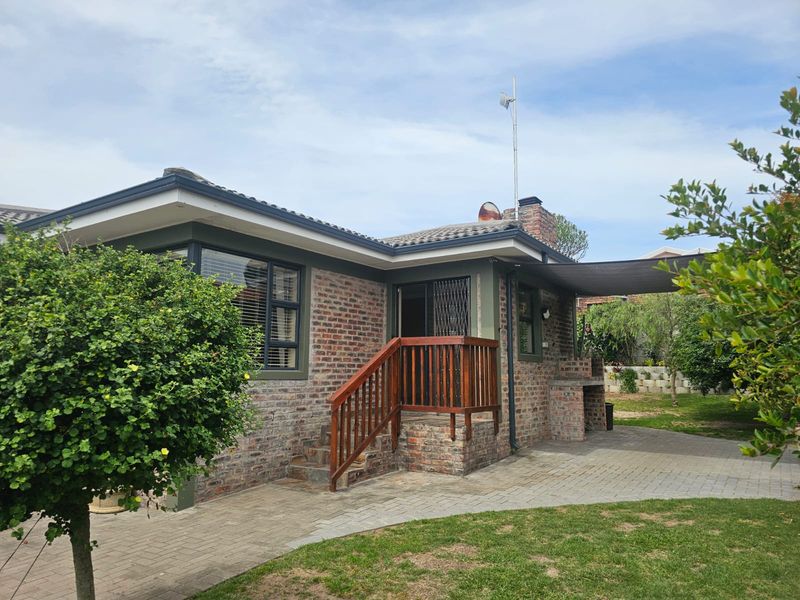 Rear view of the house featuring a face brick facade, paved patio area, built-in braai, and a wooden staircase leading to the entrance.