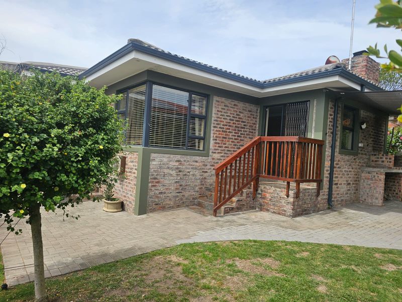 Rear exterior view featuring a face brick facade, paved patio area, timber deck with balustrade, and a built-in braai.