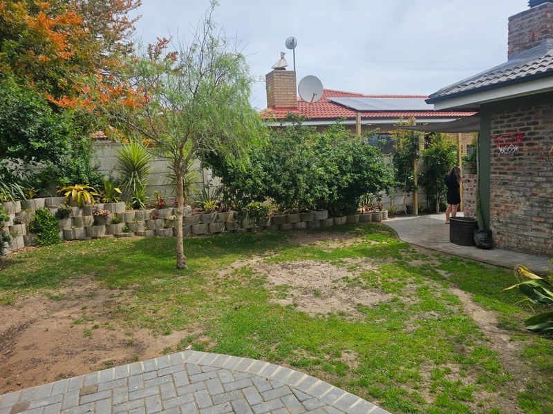 A rear garden featuring a paved patio area, brick facade, retaining wall, and established landscaping with a lawn.
