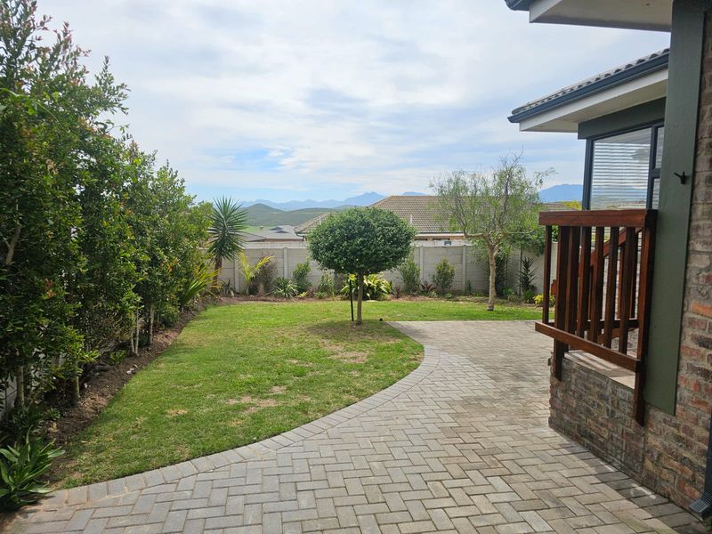 A well-maintained rear garden featuring a paved patio area, established lawn, and a secure precast boundary wall with mountain views.